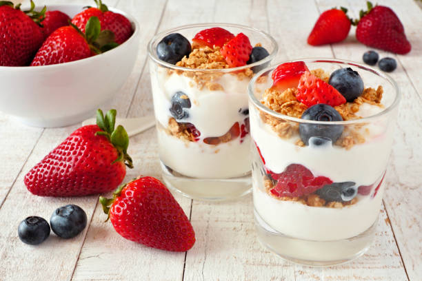 Alpro Soya Yoghurt with berries and granola in glass cups, surrounded by fresh strawberries and blueberries.
