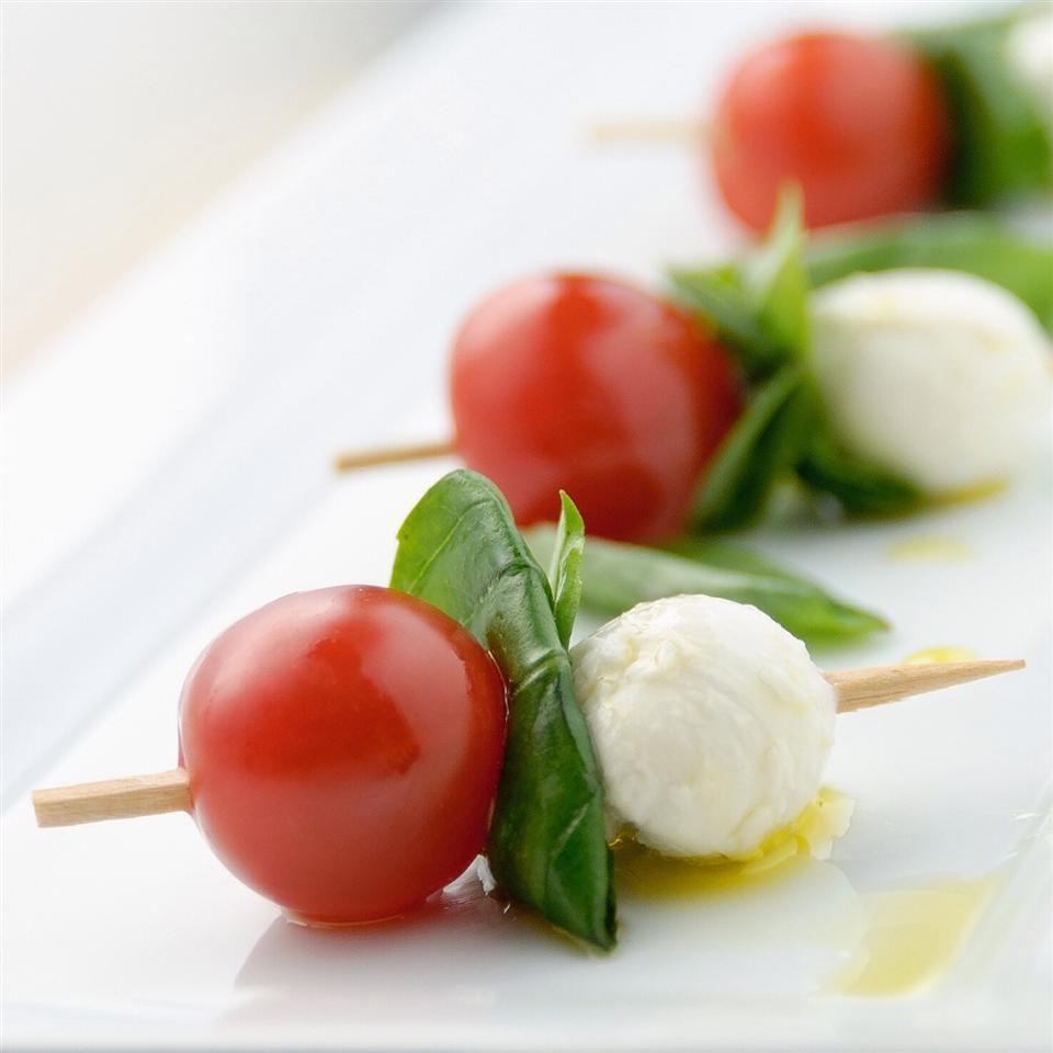 Cherry tomato and baby mozzarella sticks with basil drizzled in olive oil, served on a platter.