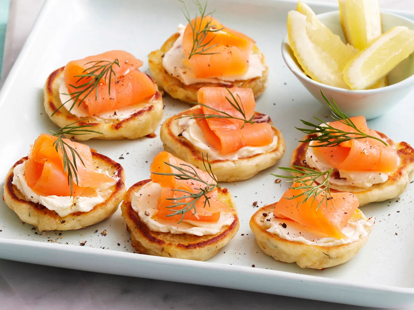 Delicious smoked salmon and cream cheese blinis served on a platter with lemon wedges and fresh dill garnish.
